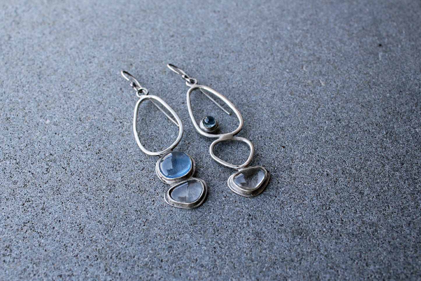 Handcrafted Armenian lightweight silver earrings featuring organic-shaped open frames and polished blue and transparent stones, handcrafted by a jewelry artisan