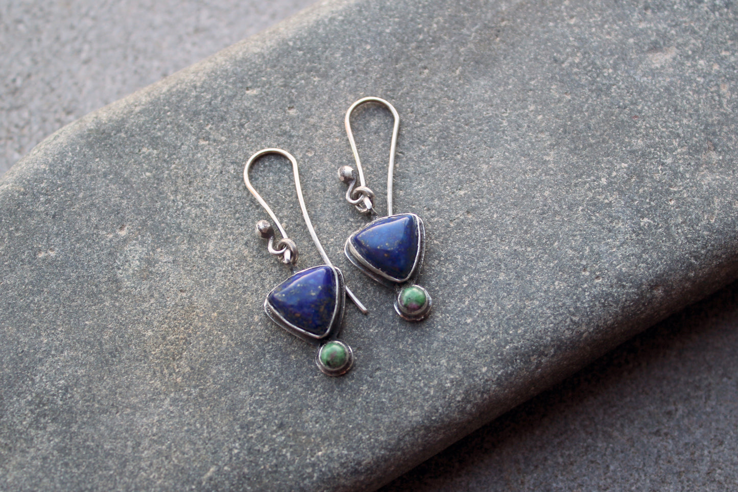 Pair of silver earrings with blue and green gemstones on a stone surface
