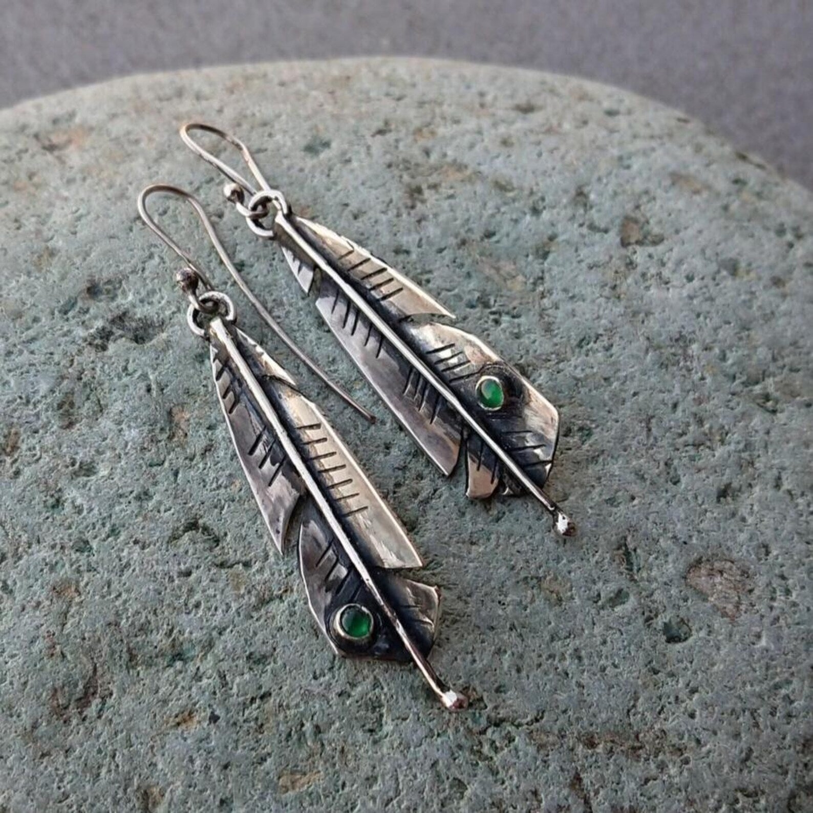 Handcrafted Armenian sterling silver artisan earrings shaped like detailed feathers, each set with small, vibrant round green onyx cabochon near the tip