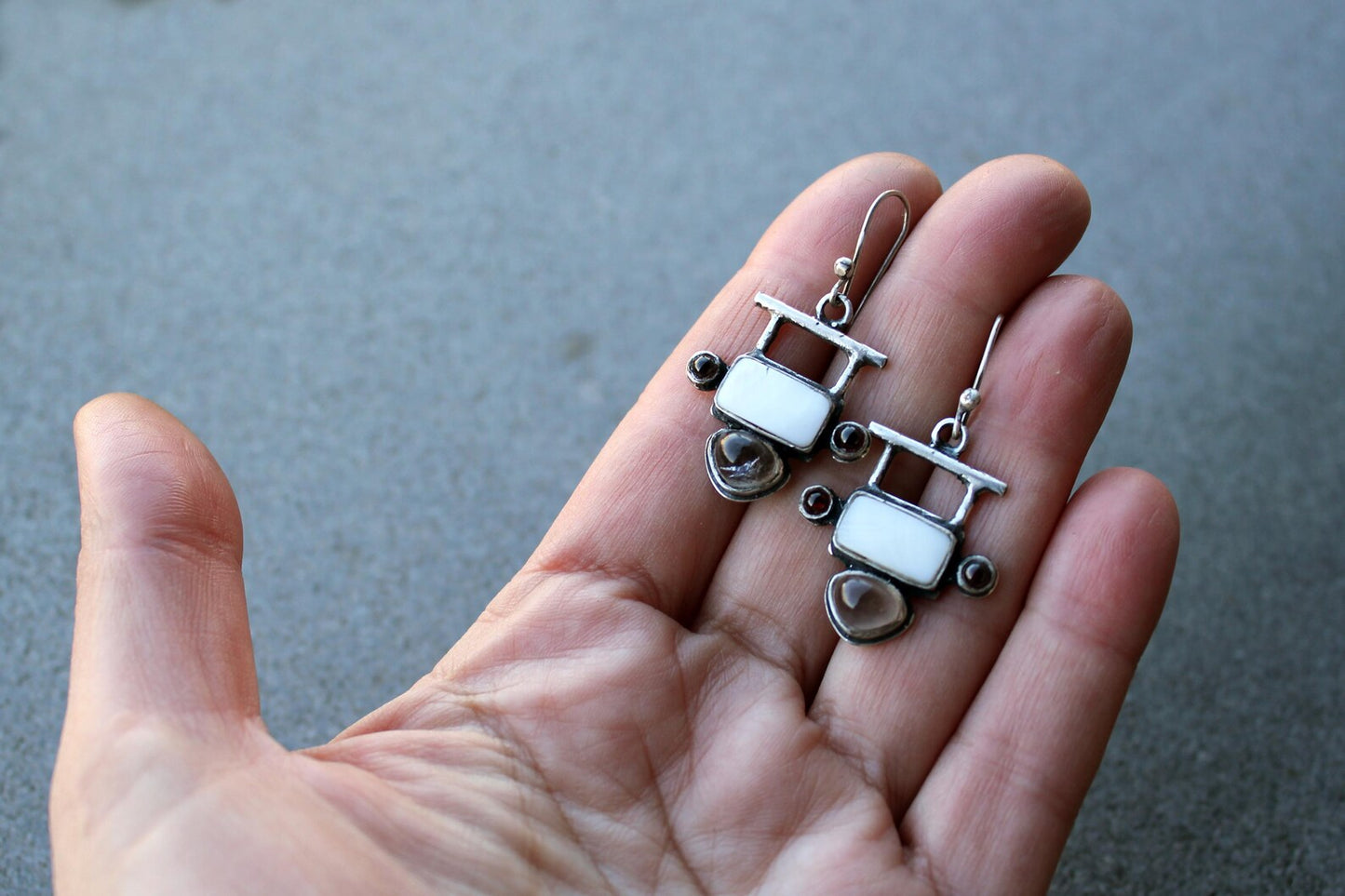 Handmade Armenian artisan sterling silver silversmith drop earrings featuring rectangular mother of pearl centers, accented by small round red garnets on the sides and teardrop-shaped grey obsidian at the base