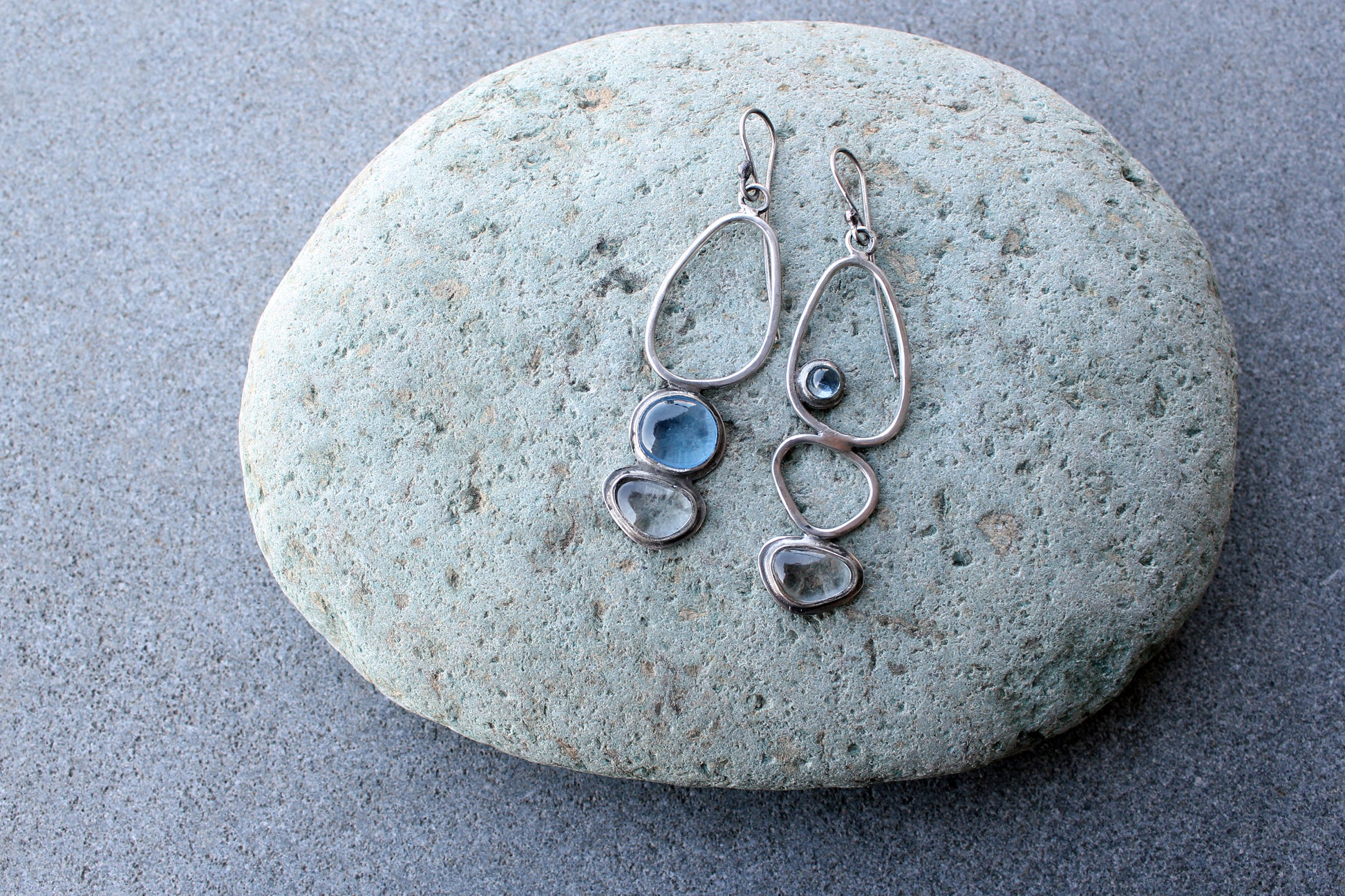 Handcrafted Armenian lightweight silver earrings featuring organic-shaped open frames and polished blue and transparent stones, handcrafted by a jewelry artisan