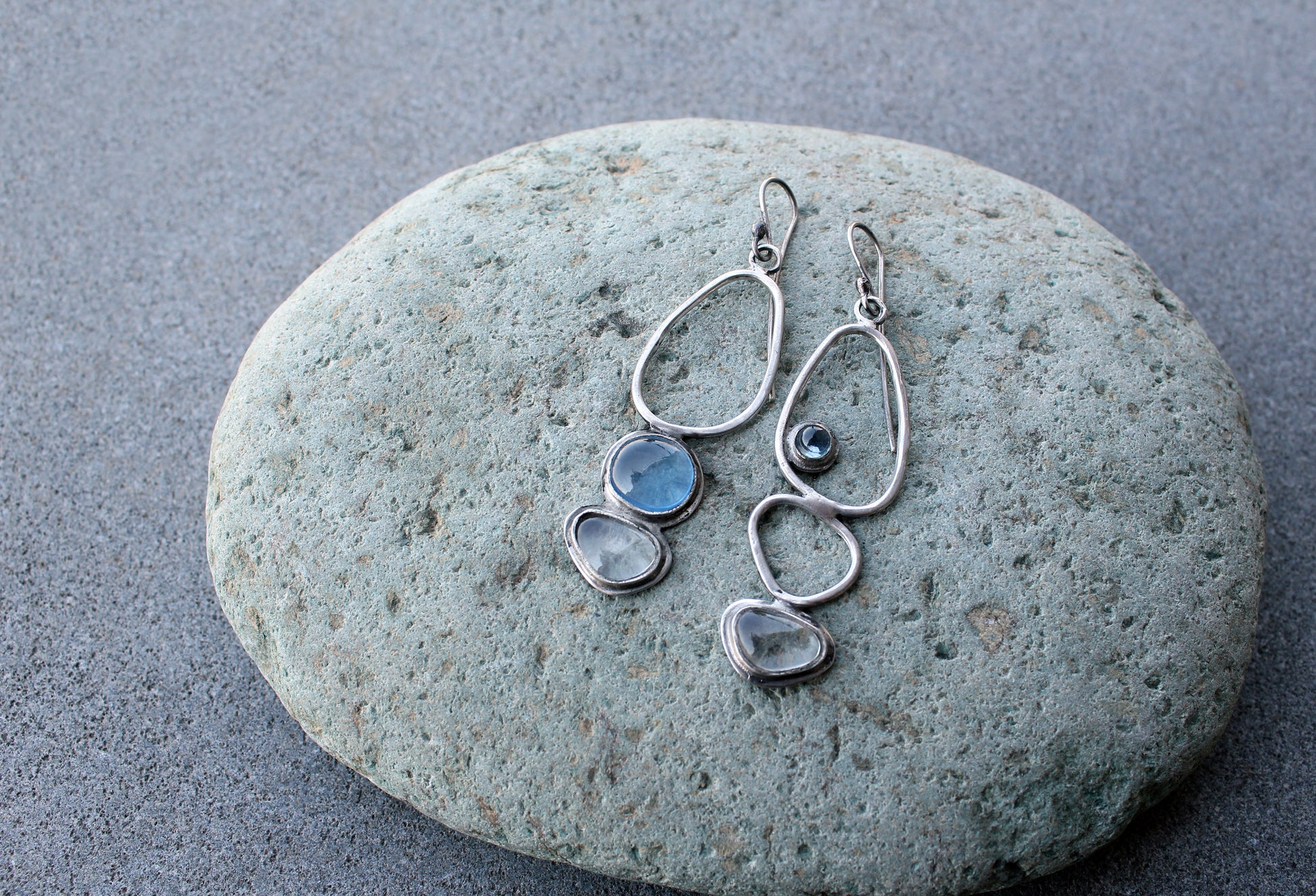 Handcrafted Armenian lightweight silver earrings featuring organic-shaped open frames and polished blue and transparent stones, handcrafted by a jewelry artisan