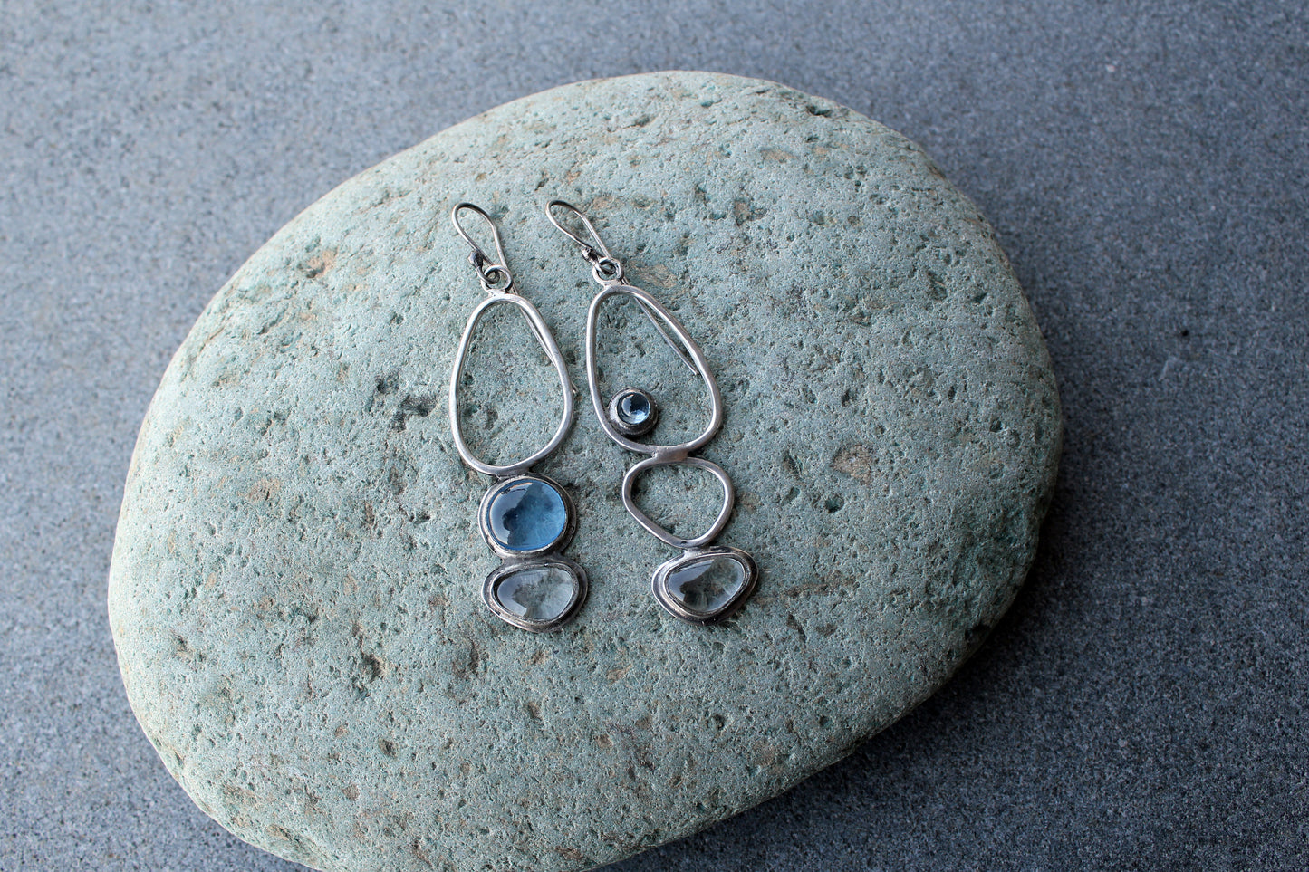 Handcrafted Armenian lightweight silver earrings featuring organic-shaped open frames and polished blue and transparent stones, handcrafted by a jewelry artisan