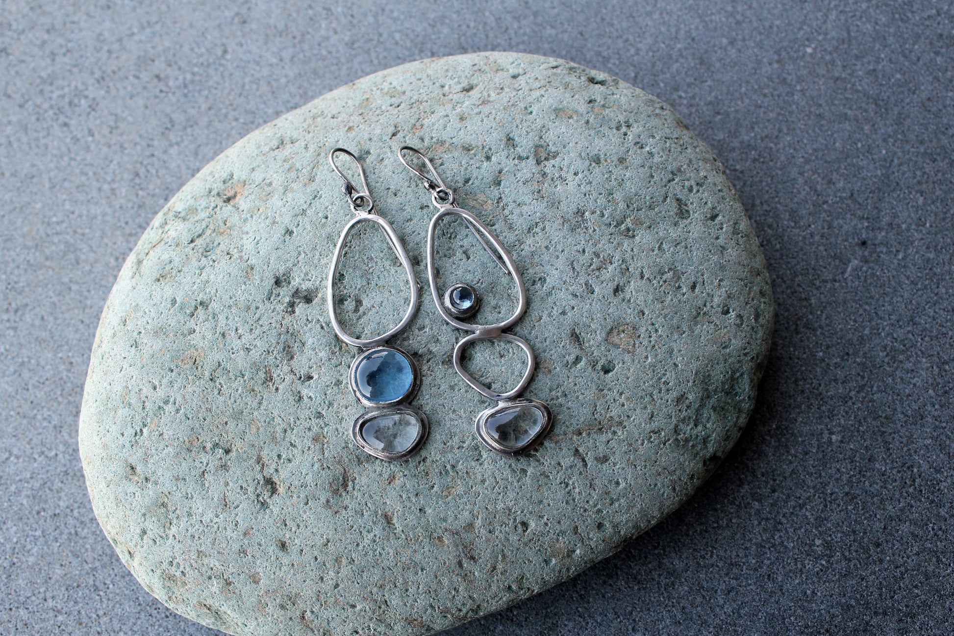 Handcrafted Armenian lightweight silver earrings featuring organic-shaped open frames and polished blue and transparent stones, handcrafted by a jewelry artisan
