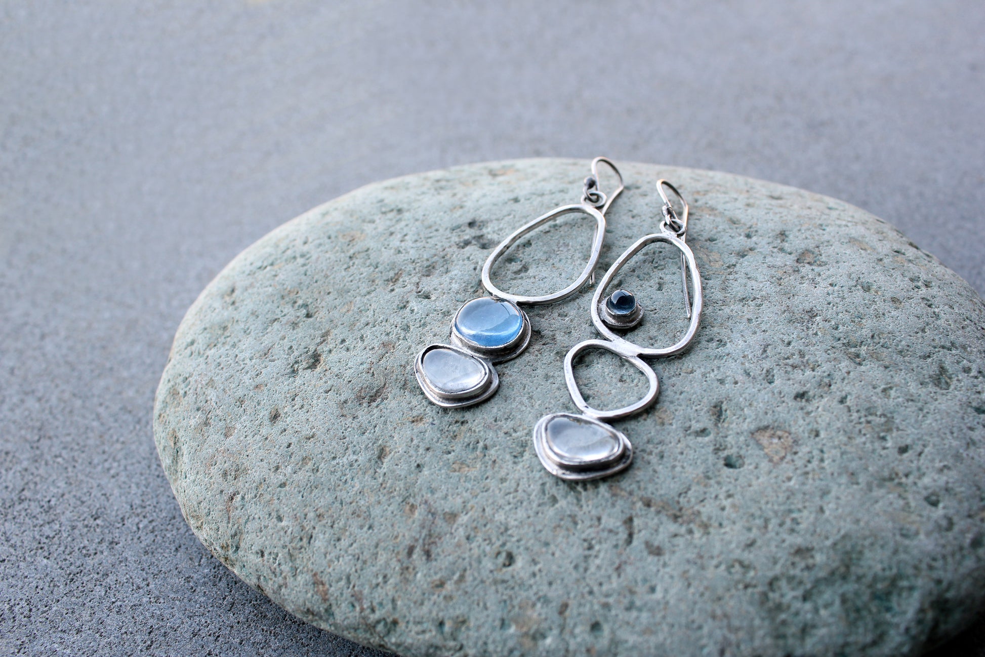 Handcrafted Armenian lightweight silver earrings featuring organic-shaped open frames and polished blue and transparent stones, handcrafted by a jewelry artisan