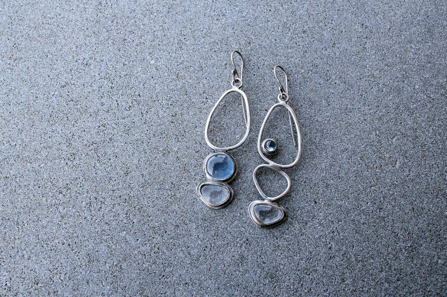 Handcrafted Armenian lightweight silver earrings featuring organic-shaped open frames and polished blue and transparent stones, handcrafted by a jewelry artisan