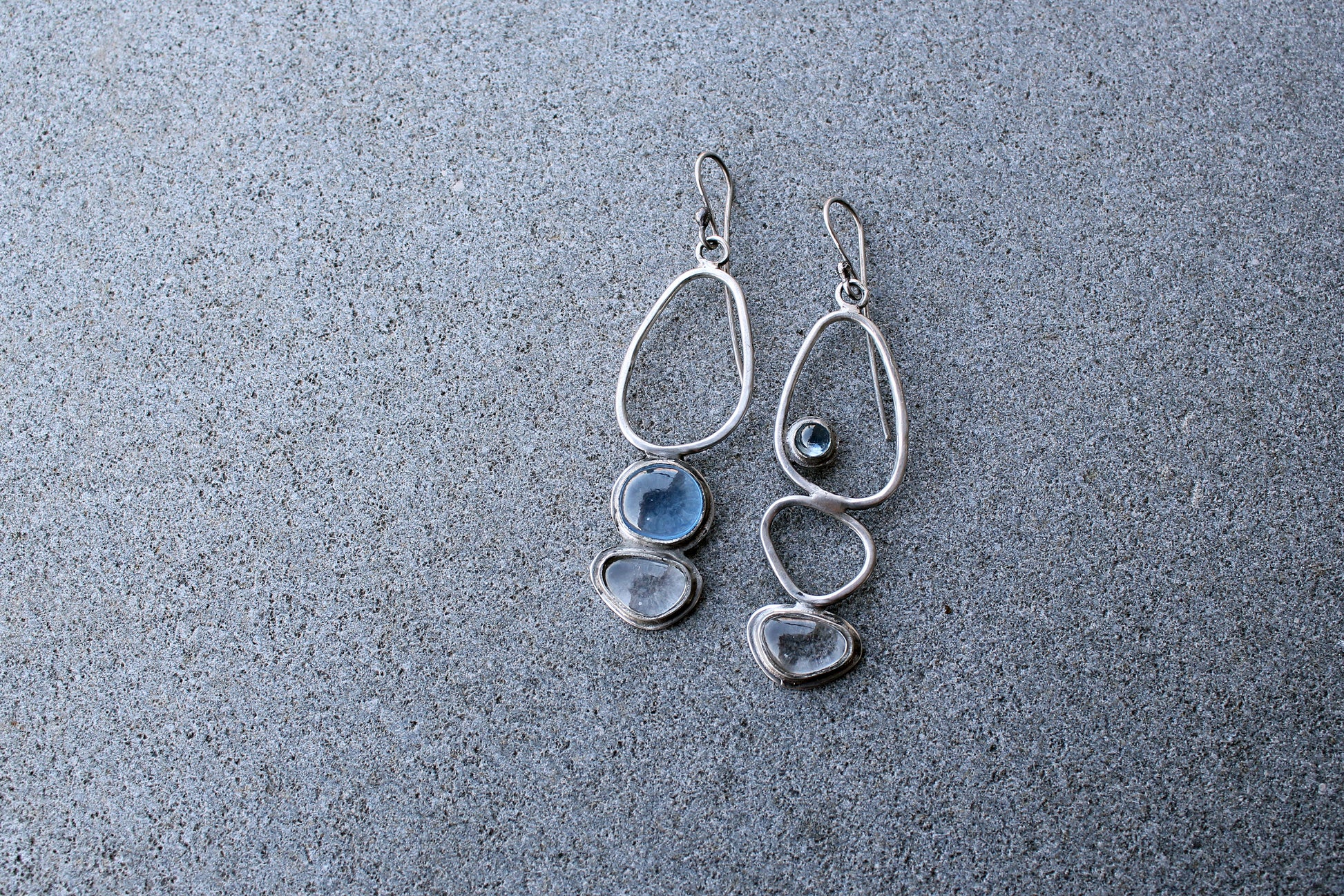 Handcrafted Armenian lightweight silver earrings featuring organic-shaped open frames and polished blue and transparent stones, handcrafted by a jewelry artisan
